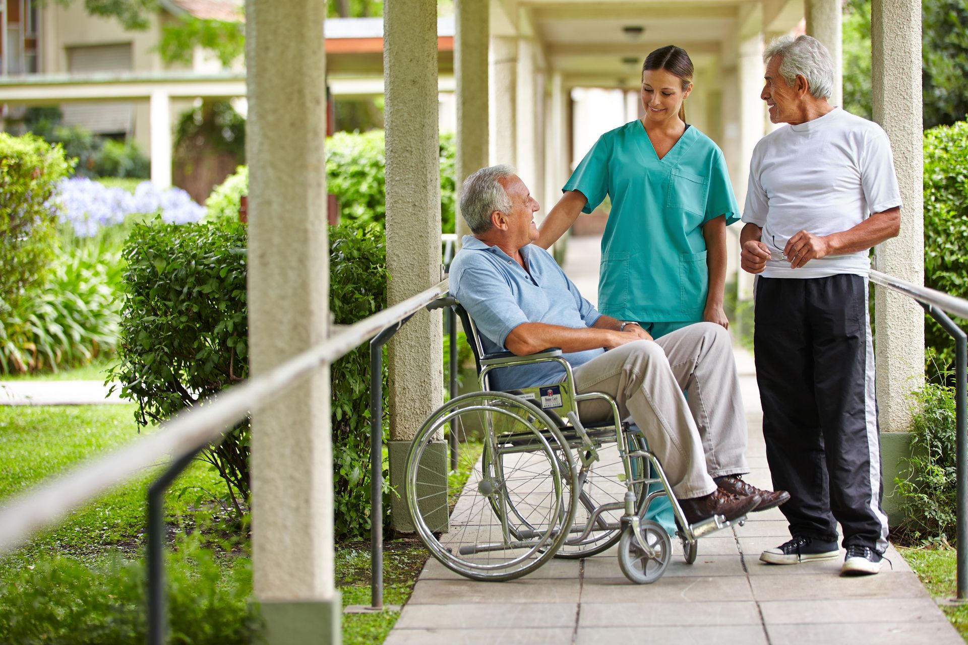 Caregiver speaking with an older adult in a wheelchair on a covered outdoor walkway