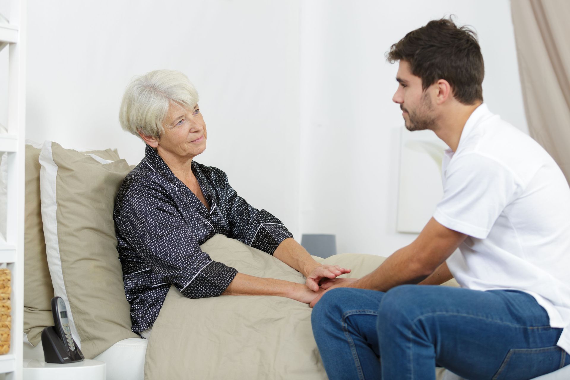 Doctor talking with a woman in a hospital bed, holding her hand in a bright room