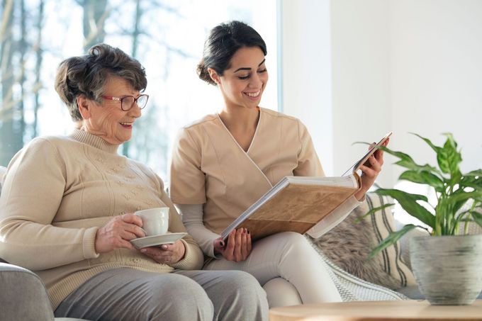 Two women reading a book together on a couch in a bright living room