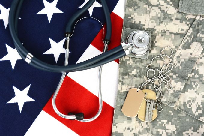 Stethoscope on American flag beside military camouflage uniform and dog tags