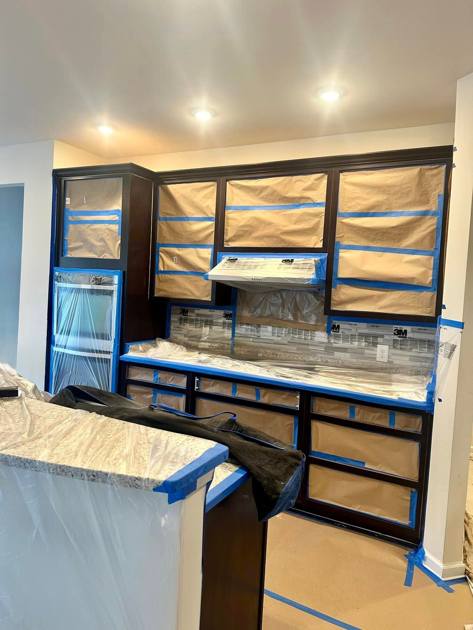 A kitchen is being painted and covered in blue tape.