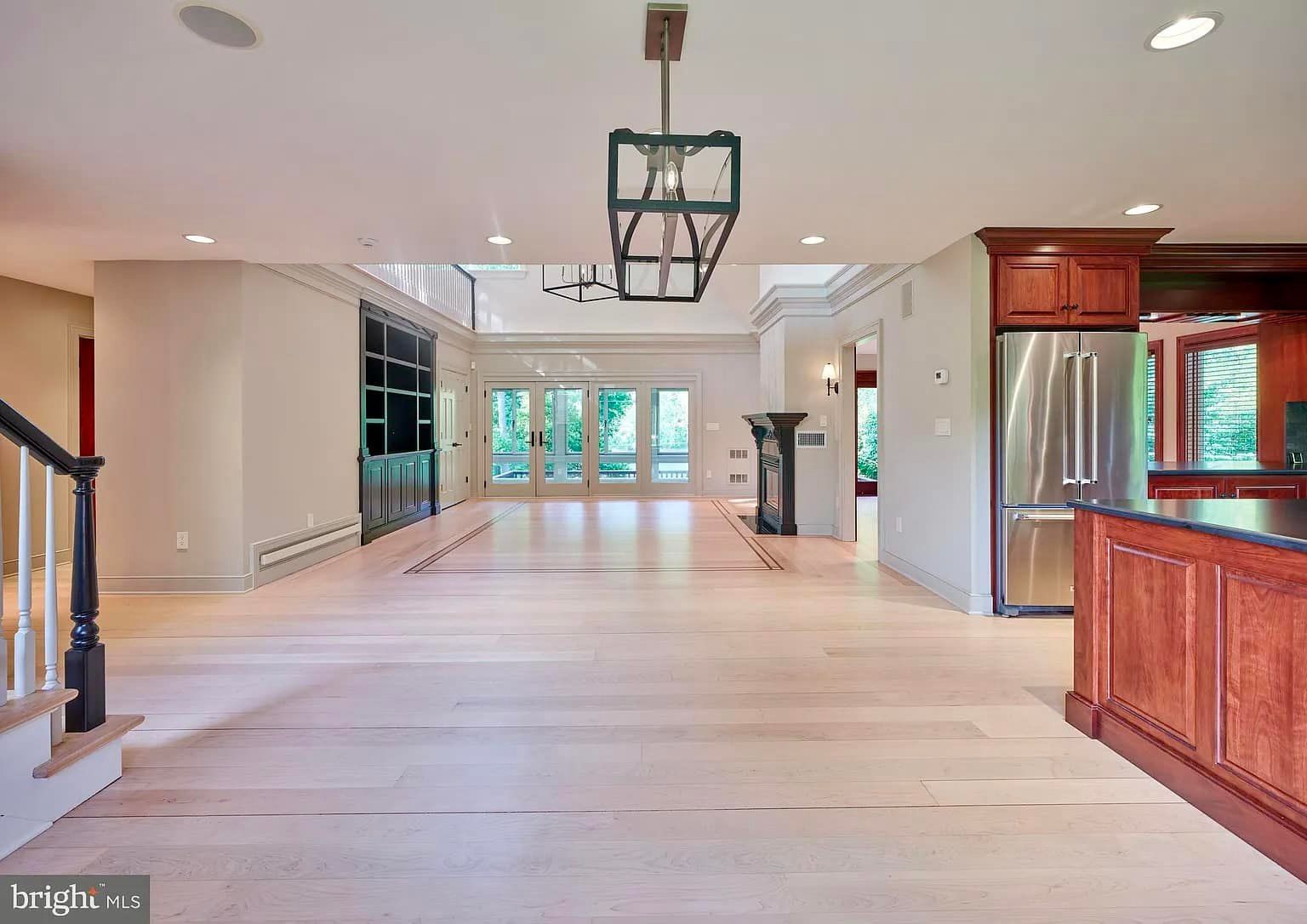 A large empty room with hardwood floors and a stainless steel refrigerator.