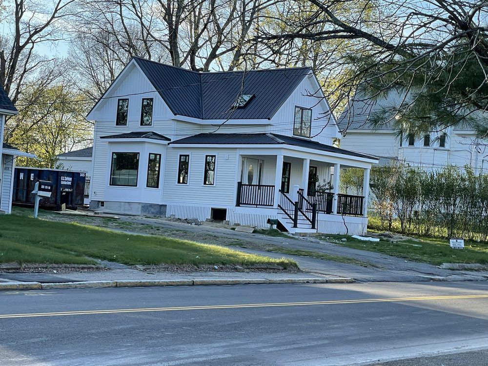 White house with black roof and porch, under construction.