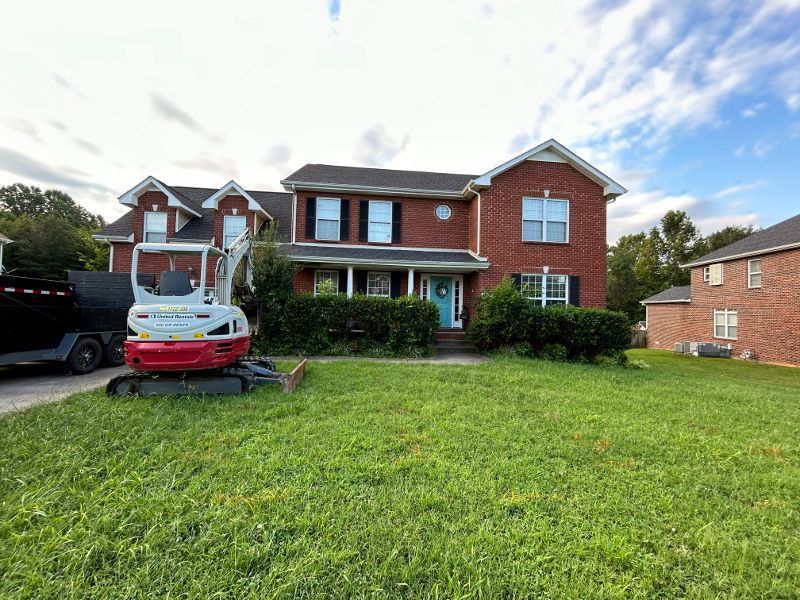 A red and white excavator is parked in front of a large brick house.