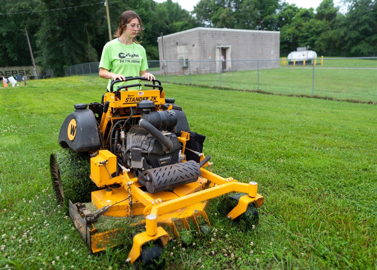 A woman is riding a yellow lawn mower on a lush green field.