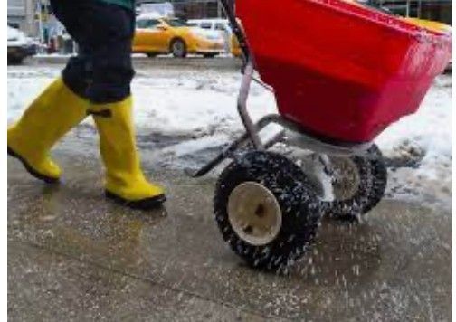 A person wearing yellow boots is pushing a wheelbarrow full of snow.