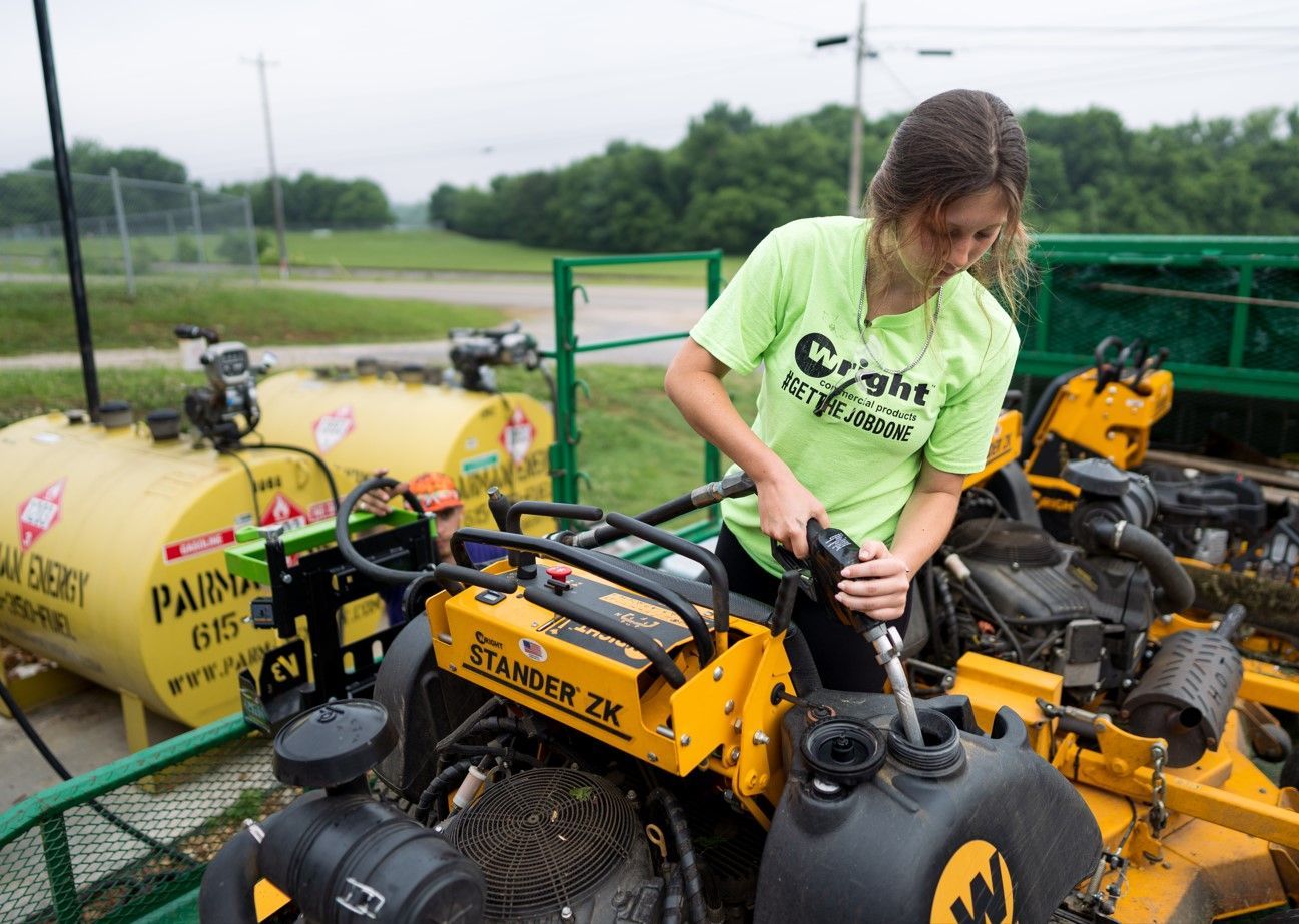 A woman in a green shirt is standing next to a yellow lawn mower.