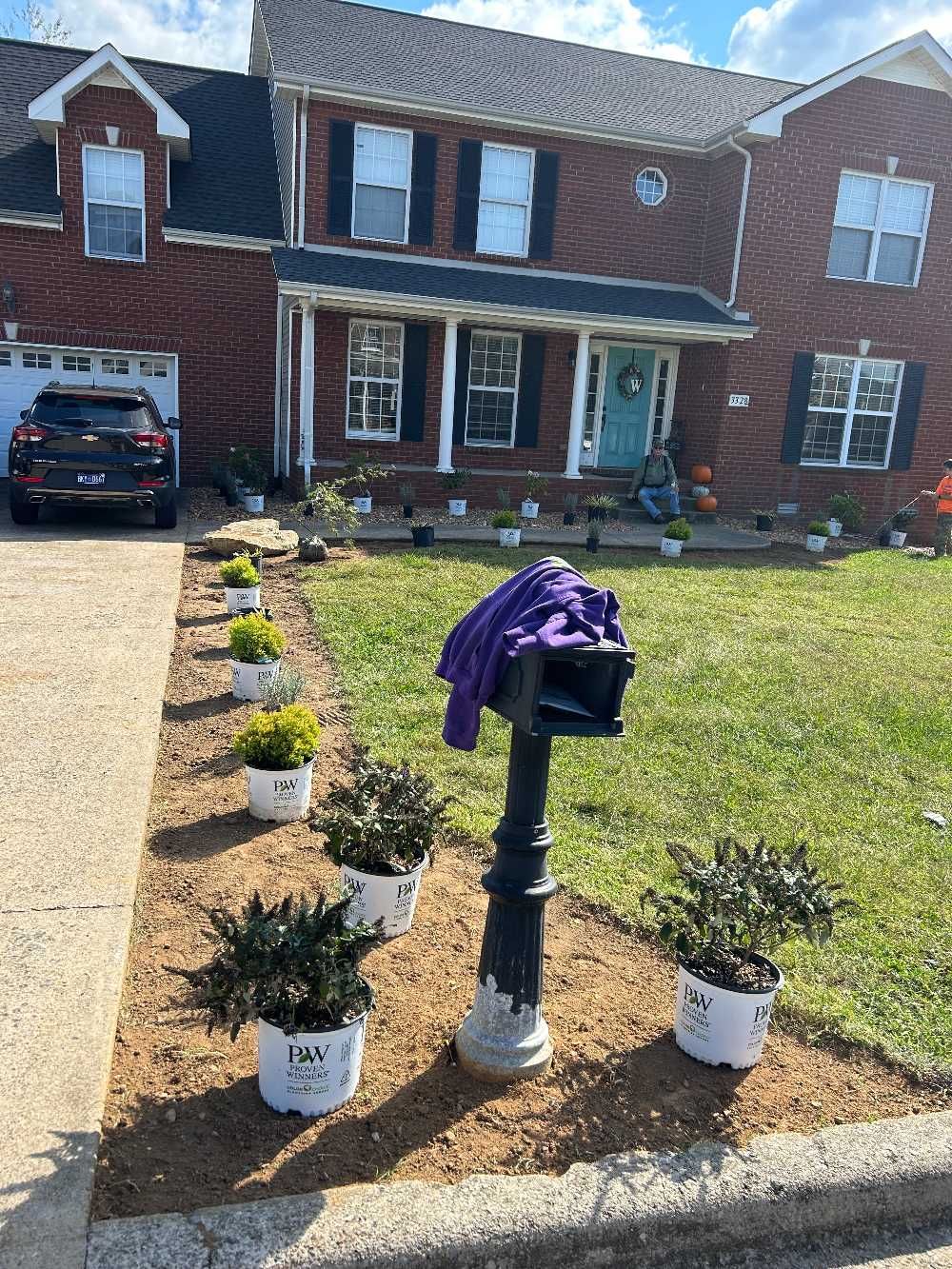 A row of potted plants are sitting in front of a brick house.