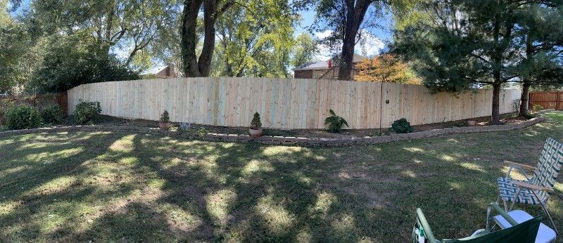 A wooden fence is surrounded by trees in a backyard.