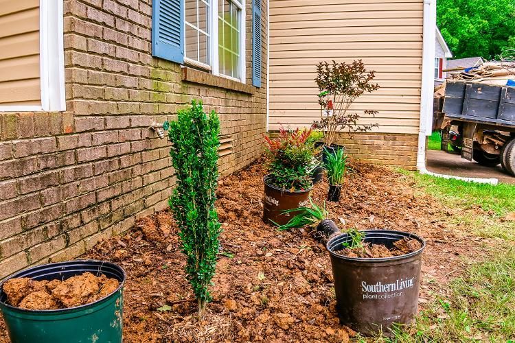 There are buckets of mulch and plants in front of a house.