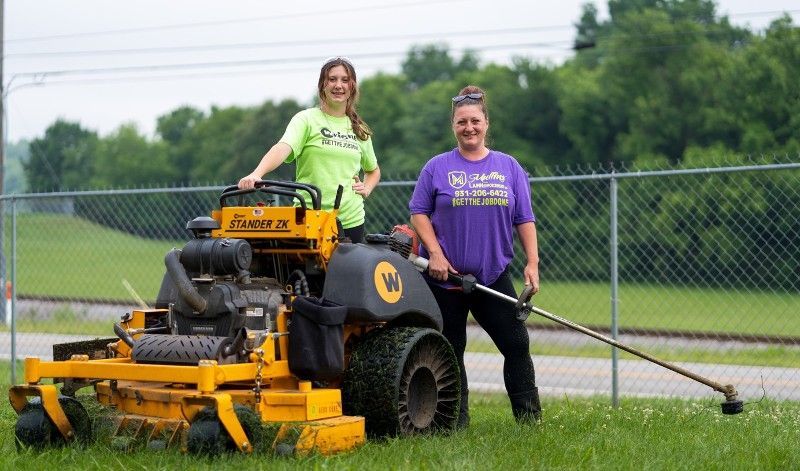 Two women are standing next to a yellow lawn mower.
