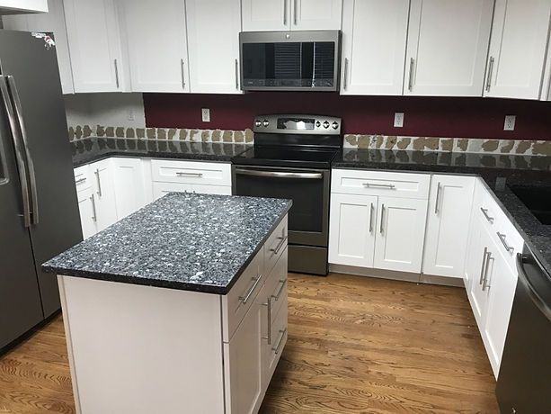 A kitchen with white cabinets , stainless steel appliances , granite counter tops and a large island.