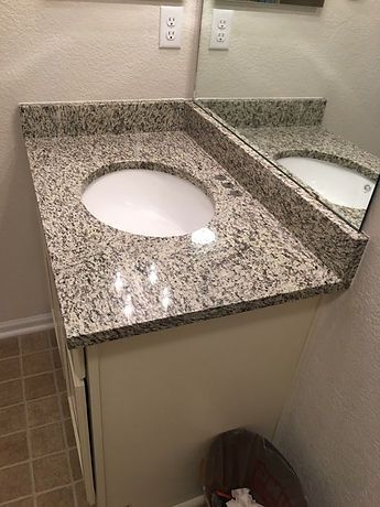 A bathroom sink with a granite counter top and a mirror.
