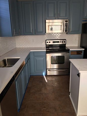A kitchen with blue cabinets , stainless steel appliances , a sink , and a stove.