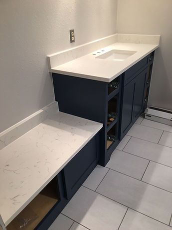 A bathroom with blue cabinets , white counter tops , and a sink.