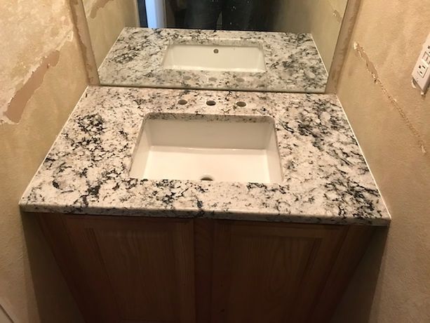 A bathroom sink with a granite counter top and a mirror.