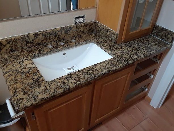 A bathroom sink with a granite counter top and wooden cabinets.