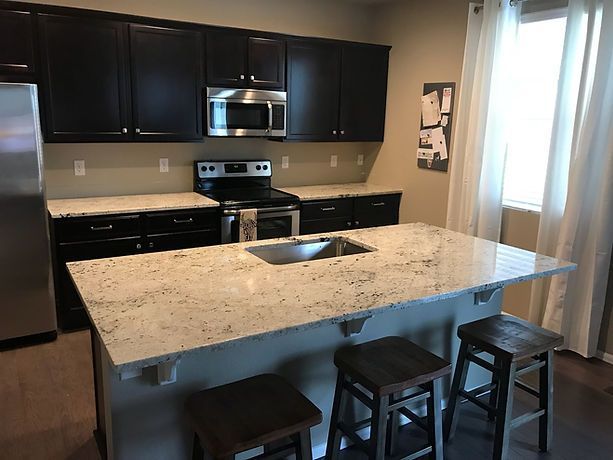 A kitchen with black cabinets , stainless steel appliances , granite counter tops and a large island.