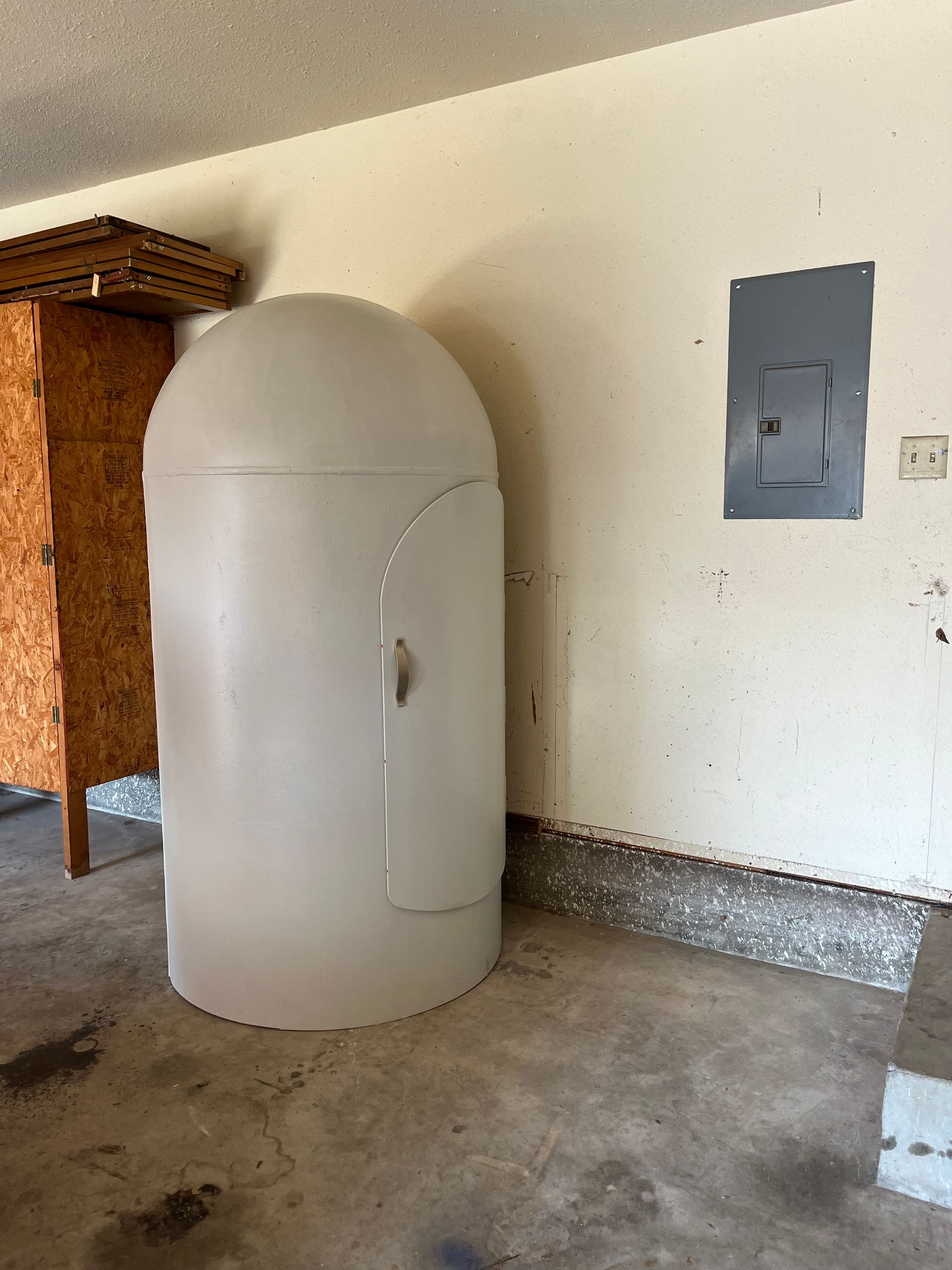 A white shelter is sitting in a garage next to a wooden cabinet.