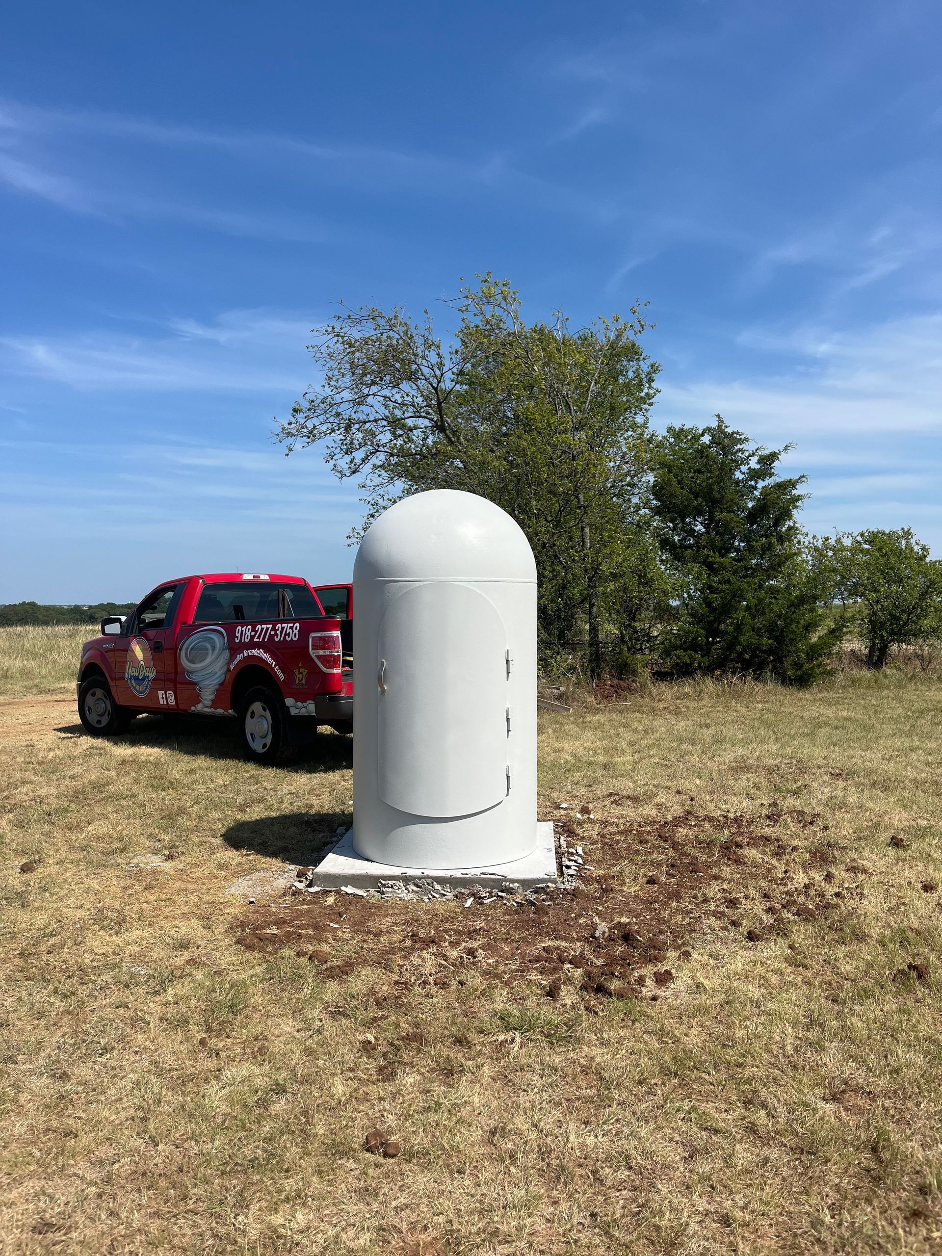 A red truck is parked next to a white cylinder in a field.