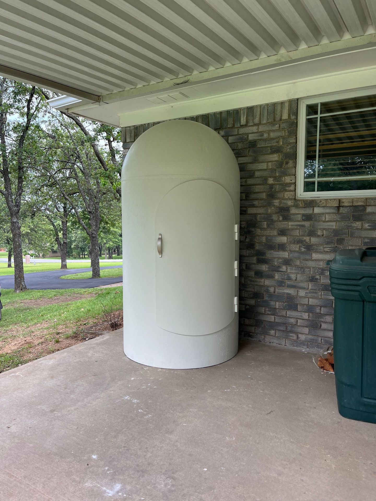 A white shelter is sitting under a covered porch next to a green trash can.