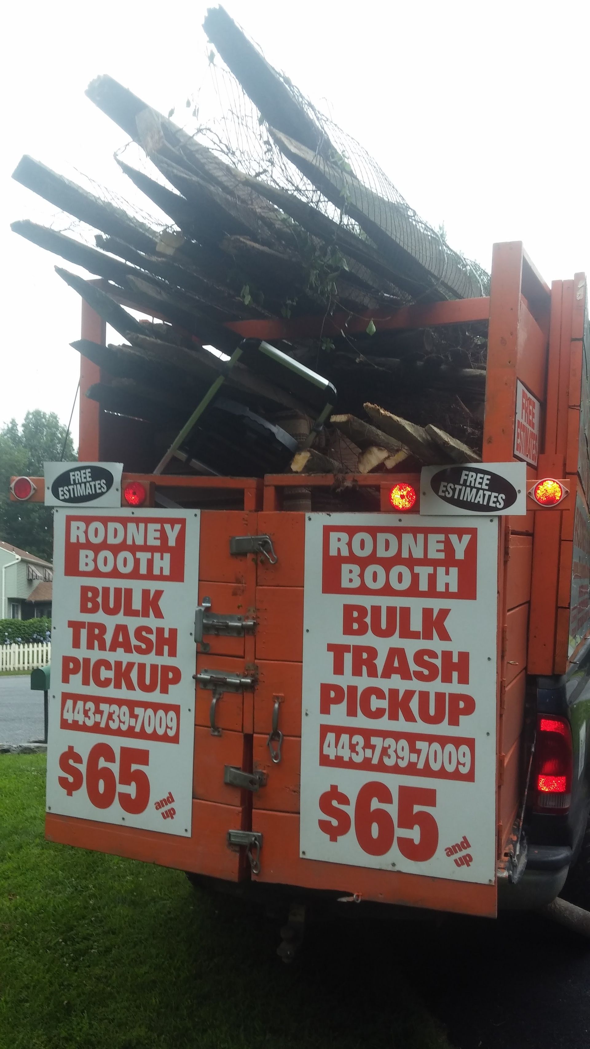 Orange dump truck loaded with scrap metal, advertising Rodney Booth Bulk Trash Pickup signs on the back