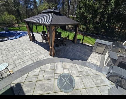 Backyard patio with stone pavers, gazebo, and grill area overlooking trees and a pool cover