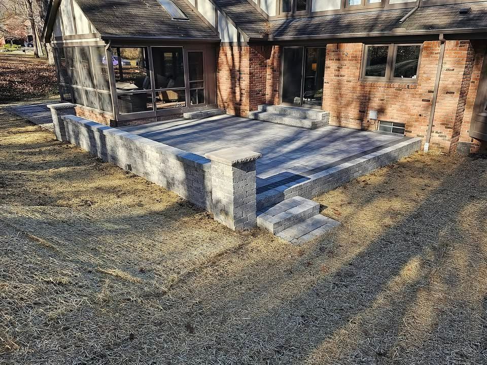 A newly constructed stone paver patio and retaining wall attached to the brick exterior of a house.