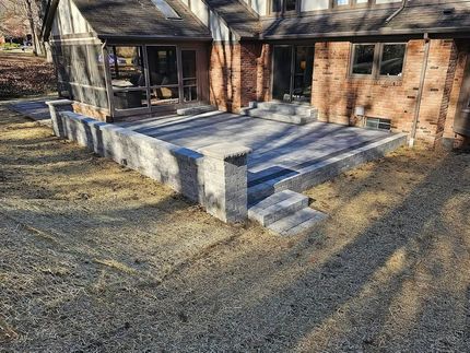 A newly constructed stone paver patio and retaining wall attached to the brick exterior of a house.