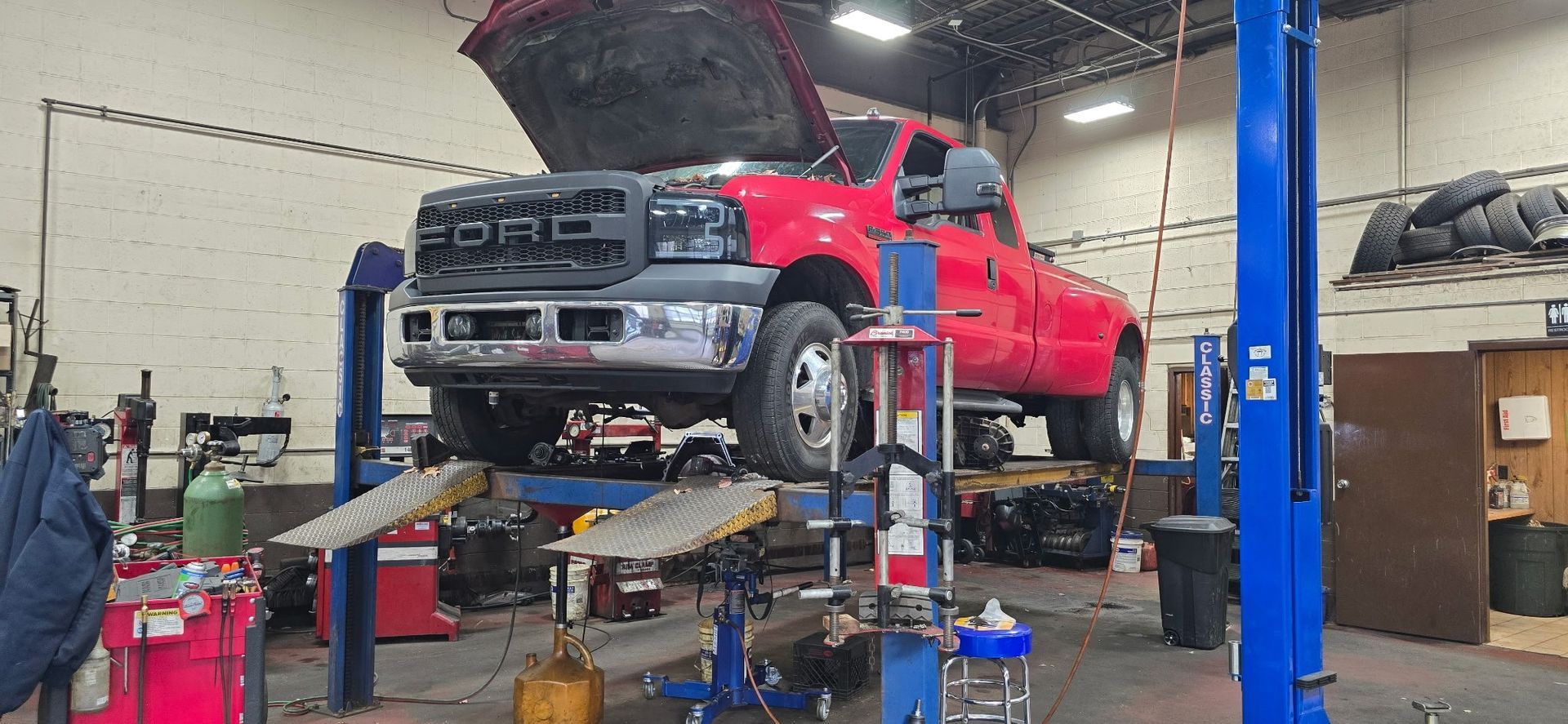 Red pickup truck raised on a lift in an auto repair shop with the hood open