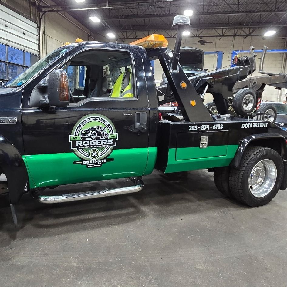 Black and green tow truck in a garage, with a lift and equipment in the bed