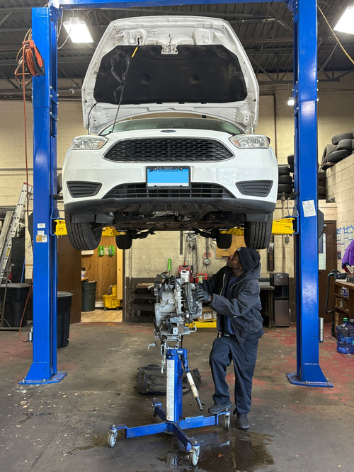 Two mechanics inspect a silver car’s open engine hood in a garage