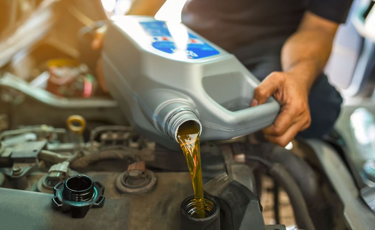 Oil being poured from a gray container into a car engine during maintenance.