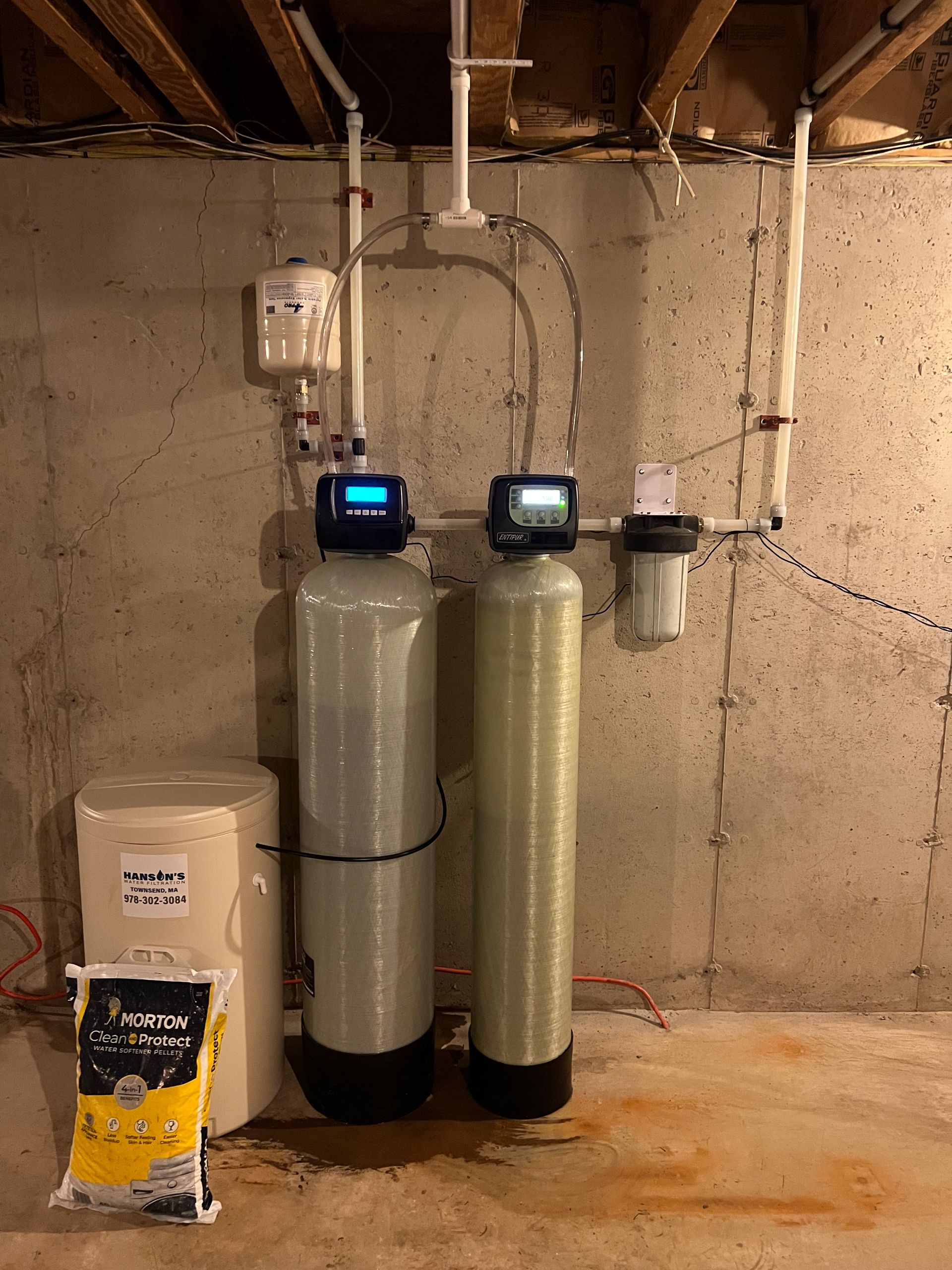 Water filtration system with two tanks, a filter, and a water softener in a basement.