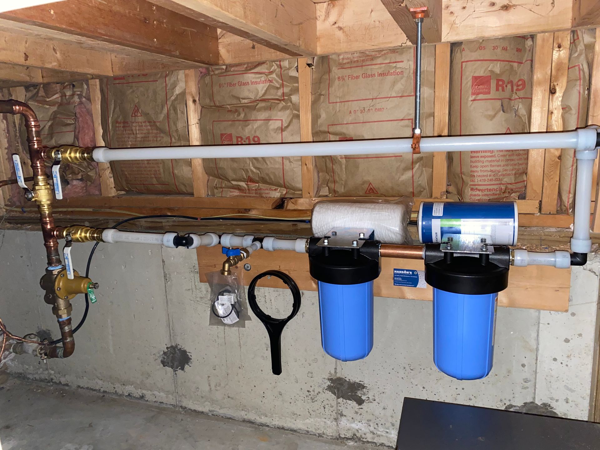 Water filtration system installed in a basement with blue filter housings and white pipes.
