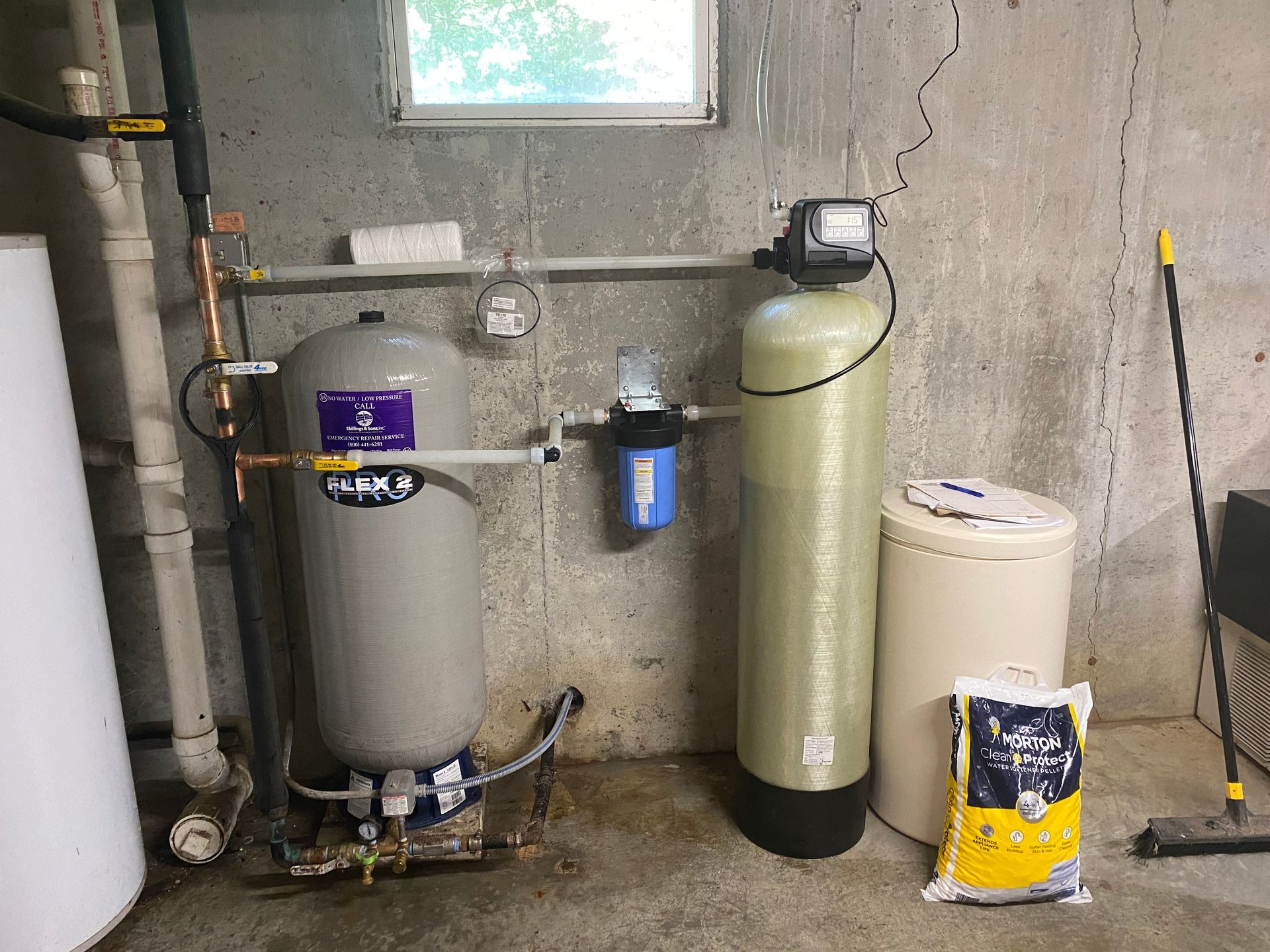Water filtration system in a basement, including a tank, filter, and salt bag.