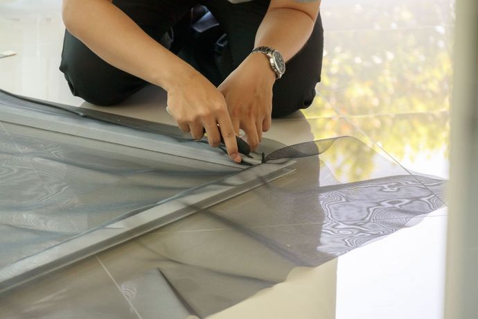 Person installing a screen, hands working on the frame. The screen is gray and the person is wearing black.