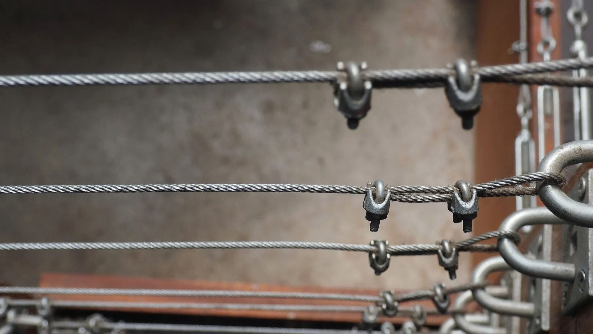 Close-up of metal wires and clamps, possibly for a clothesline, against a neutral background.
