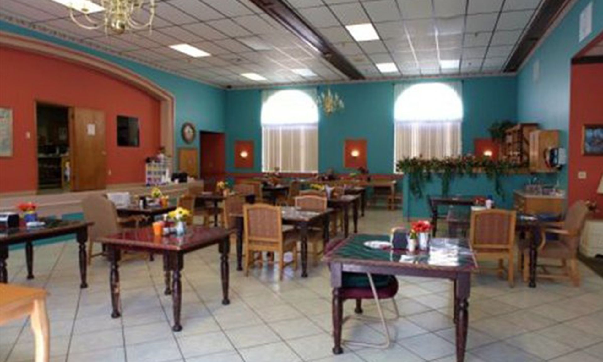 Restaurant interior with tables and chairs. Turquoise and red walls, arched windows, and tiled floor.