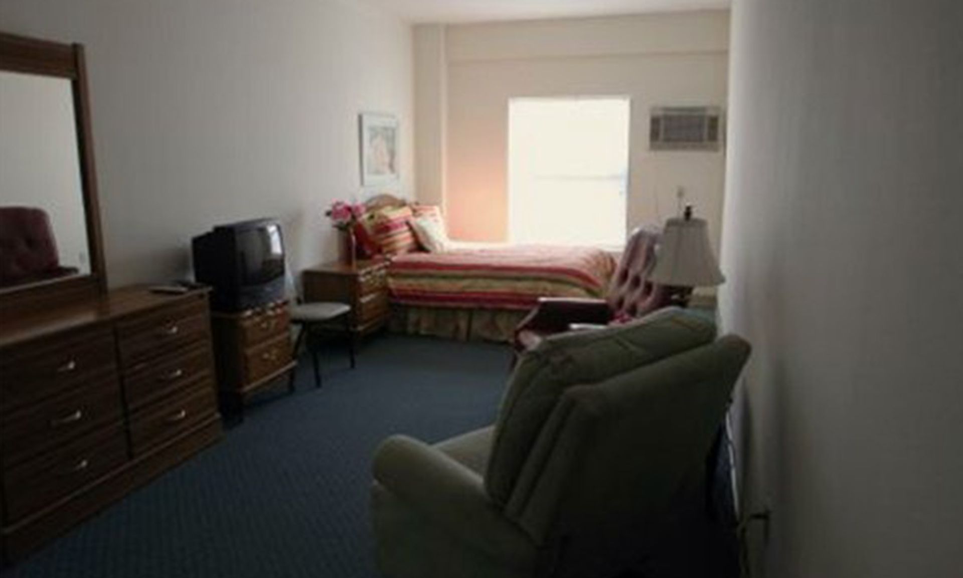 Bedroom with bed, dresser, armchair, small TV, and window.