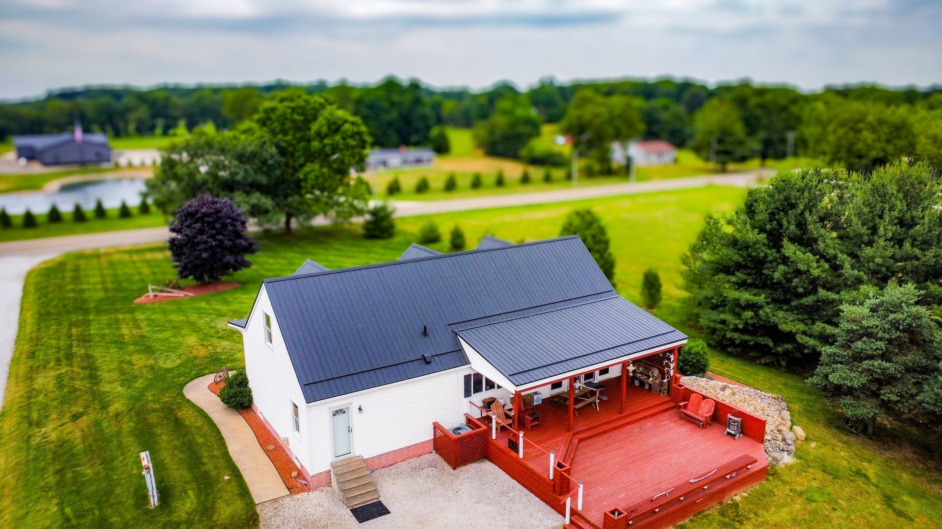 An aerial view of a white house with a black roof surrounded by trees and grass.