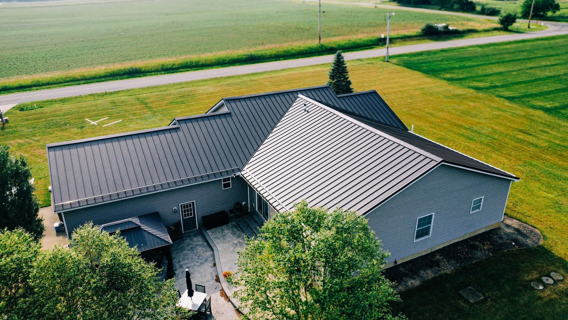 An aerial view of a house with a black roof in the middle of a field.