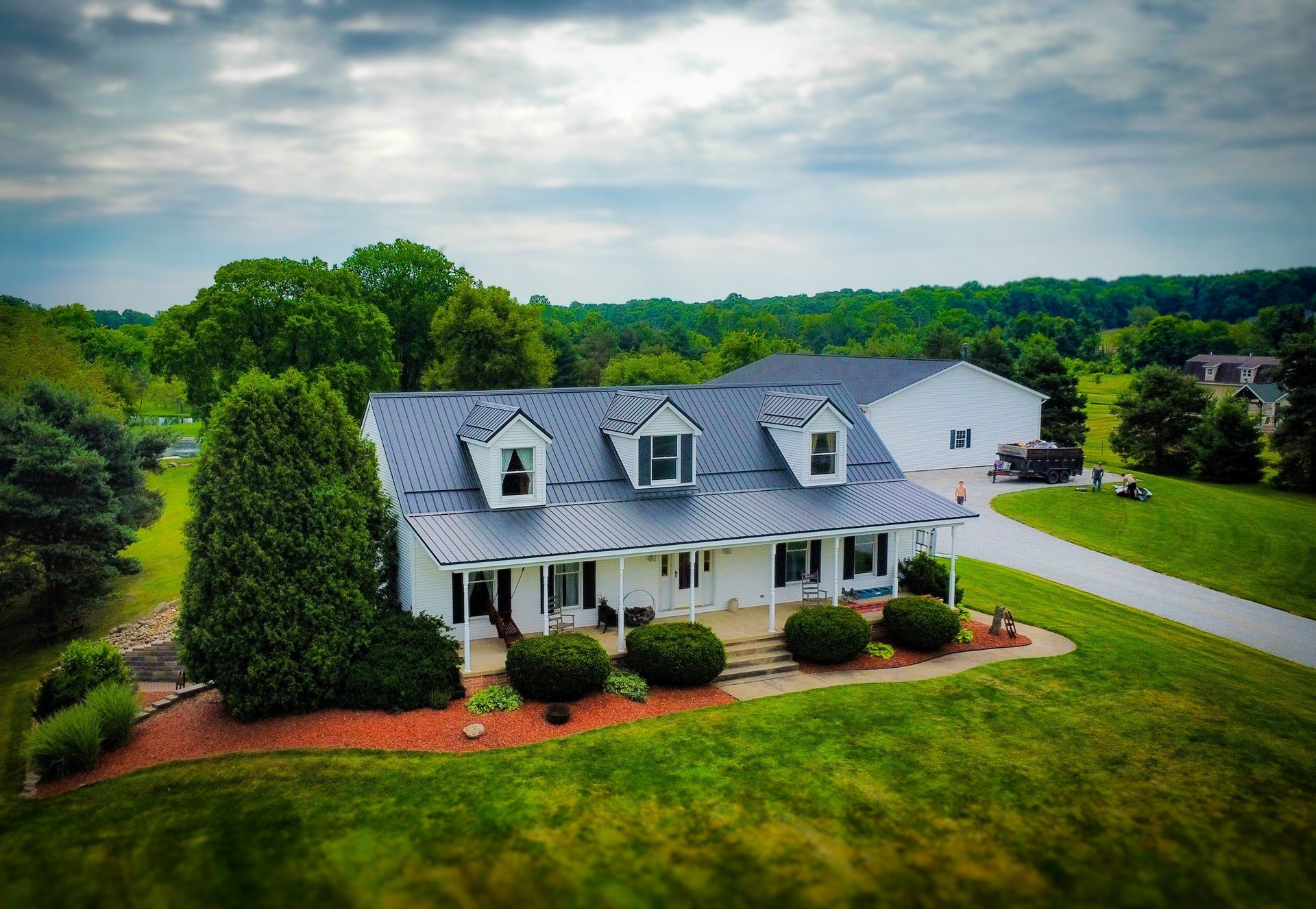 An aerial view of a large white house with a gray roof surrounded by trees and grass.