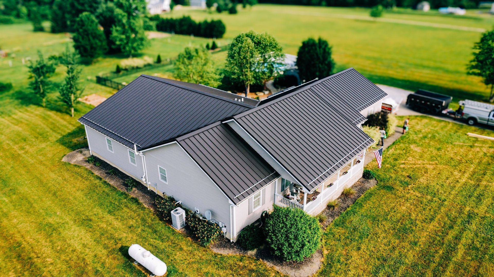 An aerial view of a house with a black roof in a grassy field.