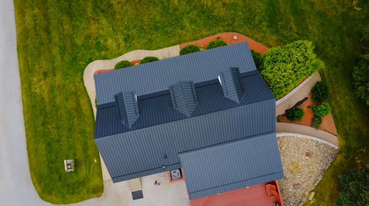 An aerial view of a house with a blue roof and a red driveway.
