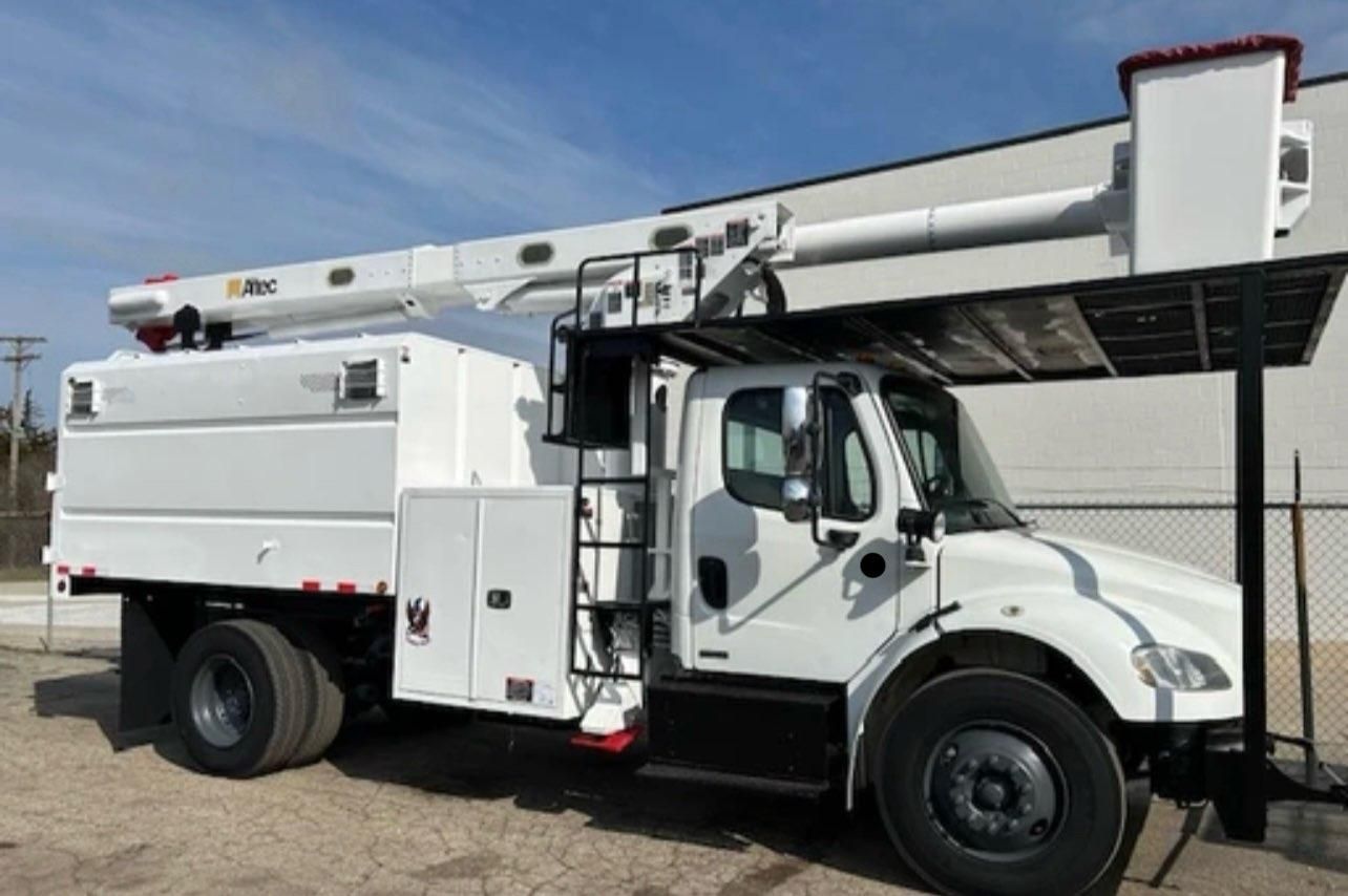 White utility truck with extended arm and bucket against a blue sky.