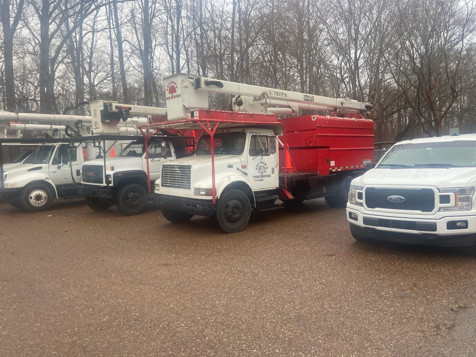 Three white utility trucks with cherry picker arms parked outside, one truck has a red cargo box.