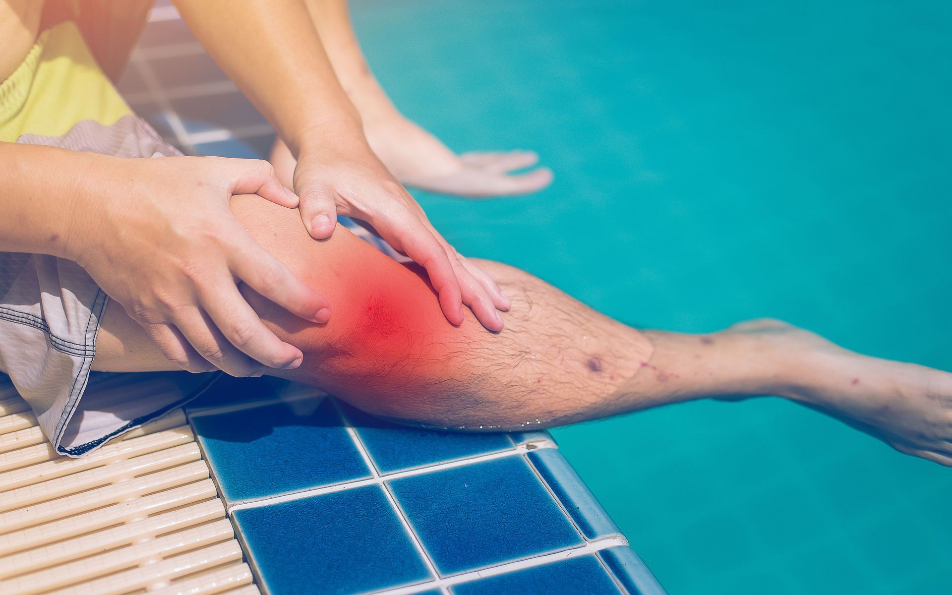 A person is checking their leg on the edge of a swimming pool.