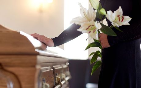 A woman is holding flowers in front of a coffin at a funeral.