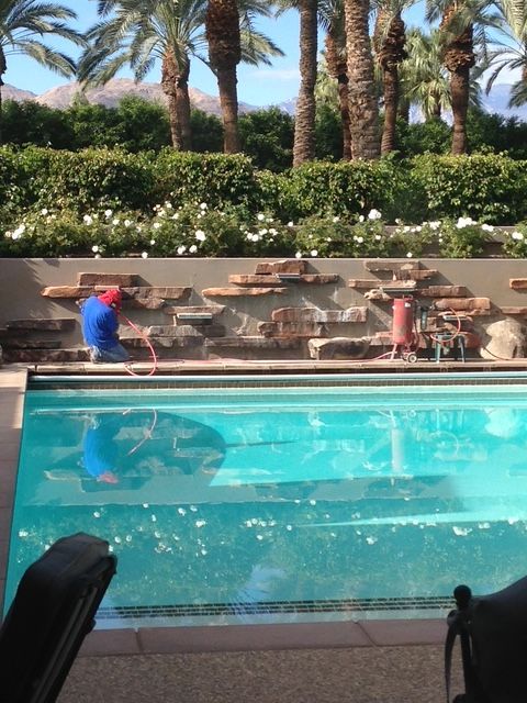 Outdoor pool with two children playing near the edge, palm trees and lounge area in the background.